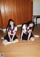 Two young women in school uniforms sitting on the floor.