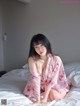 A woman in a pink robe sitting on a bed.