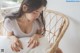 A woman sitting on a wicker chair with her hands on a pillow.