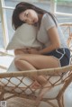 A woman sitting on a wicker chair with a pillow.