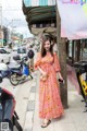 A woman in a pink dress standing on a sidewalk.