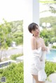 A woman in a white top and shorts posing by a pool.