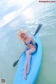 A woman in a bikini sitting on a paddle board in the ocean.