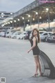 A woman in a black dress standing in a parking lot.