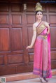 A woman in a pink and gold dress standing in front of a wooden door.