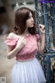 A woman in a red and white checkered top leaning against a fence.