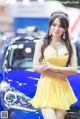 A woman in a yellow dress standing next to a blue car.