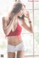 A woman in a red top and white shorts posing by a window.