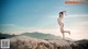 A naked woman standing on top of a large rock.