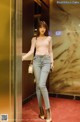 A woman standing in an elevator wearing a pink top and jeans.