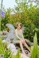 A woman in a green dress sitting on a rock in a garden.