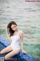 A woman in a white bathing suit sitting on the edge of a pool.