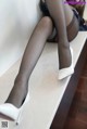 A woman in black stockings and white high heels sitting on a counter.