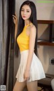 A woman in a yellow top and white skirt posing for a picture.