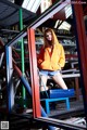 A woman in an orange hoodie sitting on a blue chair.