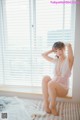 A woman sitting on a bed in front of a window.