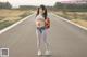 A woman standing on the side of a road holding a backpack.