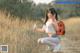 A woman crouching down in a field holding a cell phone.