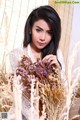 A woman in a white dress holding a bunch of dried flowers.