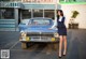 A woman standing next to a blue car in a parking lot.