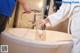 A woman in a white robe is washing her hands in a bathtub.