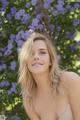 A beautiful young woman posing in front of a bush of purple flowers.