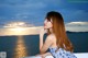 A woman in a blue and white dress sitting on a railing by the ocean.