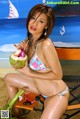 A woman in a bikini sitting on a beach chair holding a coconut.