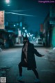 A woman in a black coat and mask standing on a street at night.