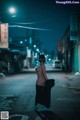 A woman in a black dress is walking down the street at night.