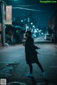 A woman wearing a cat mask walking down a street at night.