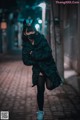 A woman wearing a black cat mask standing on a street at night.