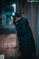 A woman wearing a black cat mask standing in an alleyway.