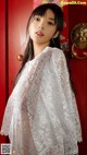 A woman standing in front of a red door wearing a white lace top.