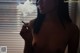 A naked woman smoking a cigarette in front of a window.