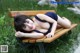 A woman laying on a wooden bench in the grass.