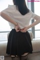 A woman in a white shirt and black skirt standing on a couch.