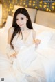 A woman in a white dress sitting on a bed.