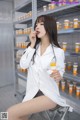 A woman sitting on a stool in front of a shelf of pills.