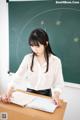 A woman sitting at a desk in front of a blackboard.