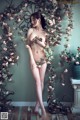 A naked woman standing in front of a wall of flowers.