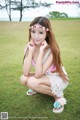 A woman in a pink bikini sitting on the grass.