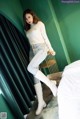 A woman in a white sweater and jeans posing on a bed.