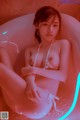 A woman in a white bikini sitting in a bathtub.