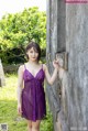 A woman in a purple dress leaning against a stone wall.