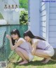 A couple of young women sitting next to each other near a fence.