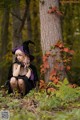 A woman dressed as a witch sitting in the woods.