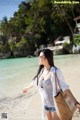 A woman walking on a beach with a straw bag.