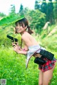 A woman in a plaid skirt holding a gun in a field.